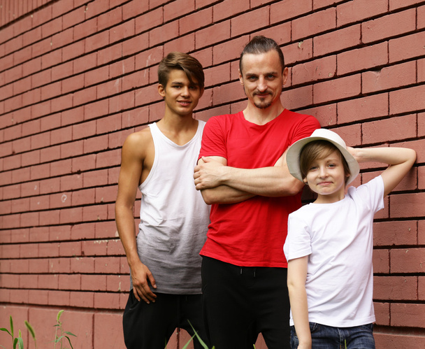 family, father and two sons having fun and posing brick wall background - 写真・画像