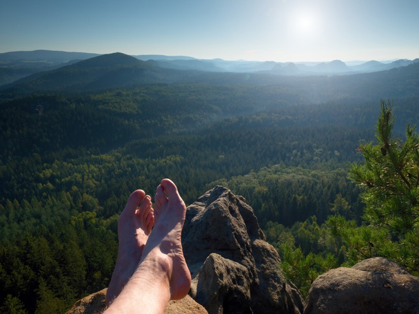 Las piernas desnudas masculinas peludas descansan en el pico de la roca. Actividades al aire libre en verano. Valle de bosque largo en landscae montañoso del parque natural
. - Foto, imagen