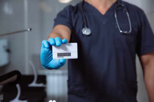 mannelijke arts tonen visitekaartje en camera kijken - Foto, afbeelding