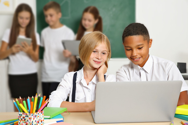 Schoolchildren sitting in classroom with laptop - Fotó, kép