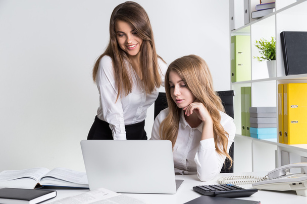 Two young businesswomen in office. They are looking at laptop screen. One is smiling. Concept of trainee in big company - Φωτογραφία, εικόνα