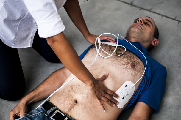 girl applying defibrillator pads to an unconscious guy - Photo, Image