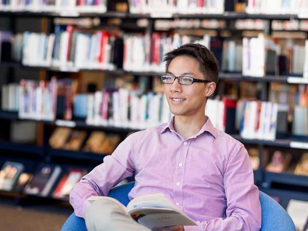 Щасливий студент чоловічої статі тримає книги в бібліотеці
 - Фото, зображення