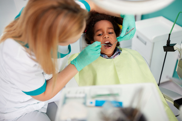 Female dentist repair tooth to nice black kid  - Фото, изображение