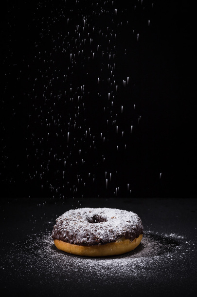 Sprinkling sugar powder on chocolate donut  - Foto, afbeelding
