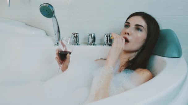 Girl with red wine glass in bath full of foam. Smoking electronic cigarette. - Video, Çekim