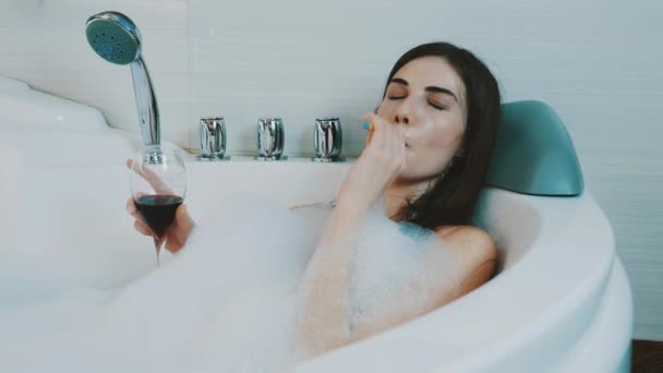Girl drink red wine in bath full of foam. Smoking electronic cigarette. Resting - Záběry, video