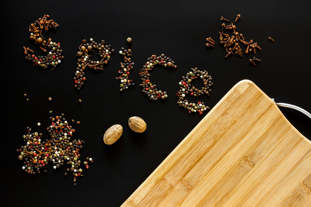 Food background. Spice written pepper, carnation, nutmeg and empty cutting board with blank space for mock up on black chalkboard. Topview. Mockup. Flatlay. - Photo, Image
