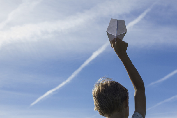 Kağıt Uçak mavi gökyüzü karşı elinde bir çocuk. Düşük açılı görünüş - Fotoğraf, Görsel