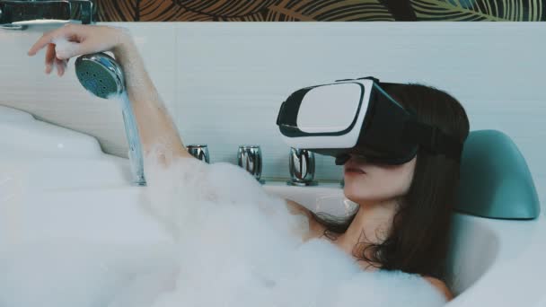 Chica tomar un baño lleno de espuma en el baño. Mirando en gafas de realidad virtual
. - Metraje, vídeo