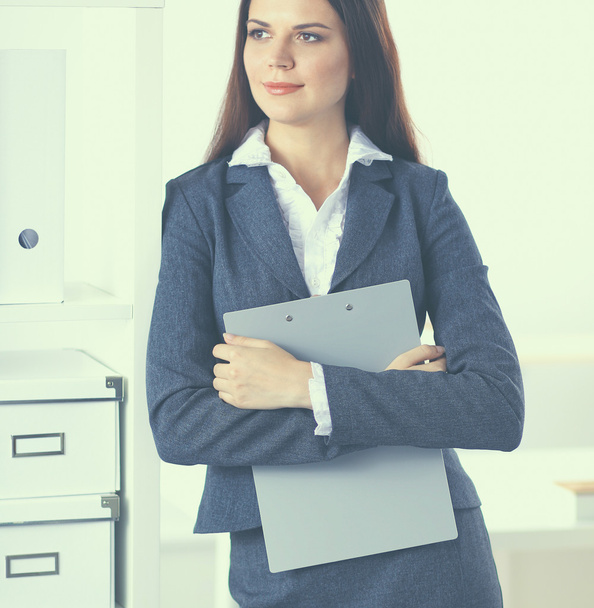 Attractive young businesswoman standing near desk with folder in the office - Foto, afbeelding