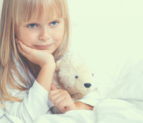 Little girl with teddy bear lying on the bed at home - Fotografie, Obrázek