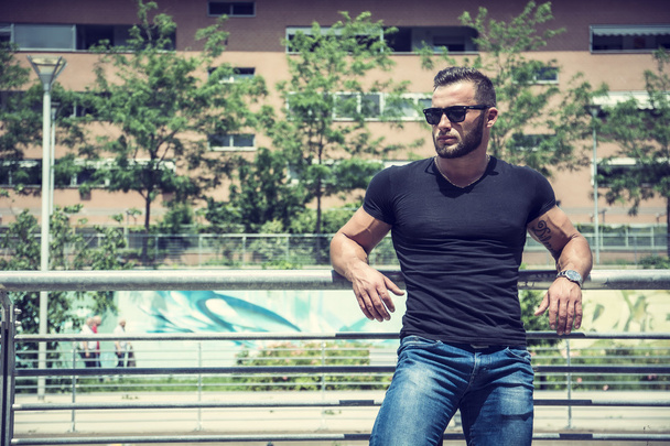 Handsome muscular man standing in city setting - Foto, afbeelding