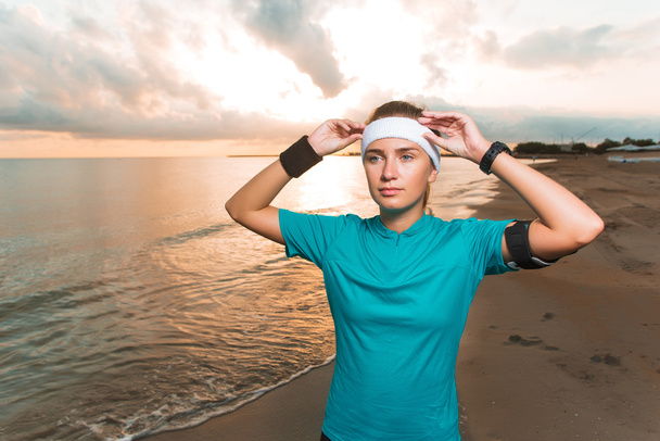 Young sporty girl doing morning exercises on beach at sunrise - Фото, изображение