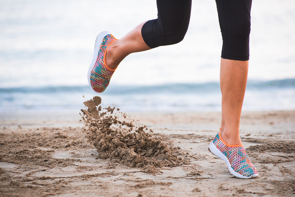 Крупним планом жіночі ноги біжать на пляжі під час сходу сонця вранці з піском в русі
 - Фото, зображення