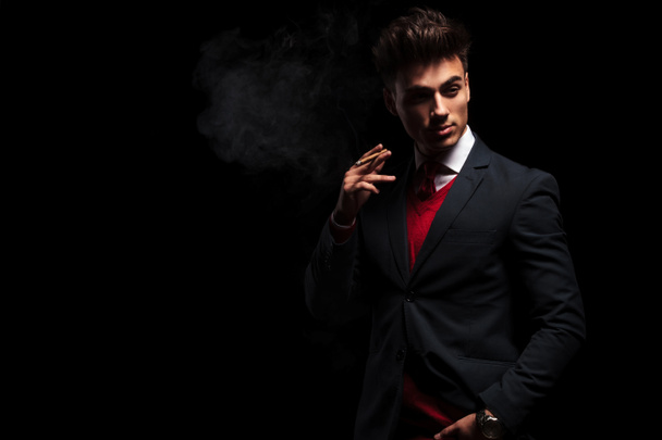 elegant young businessman standing and smoking in studio - Photo, Image