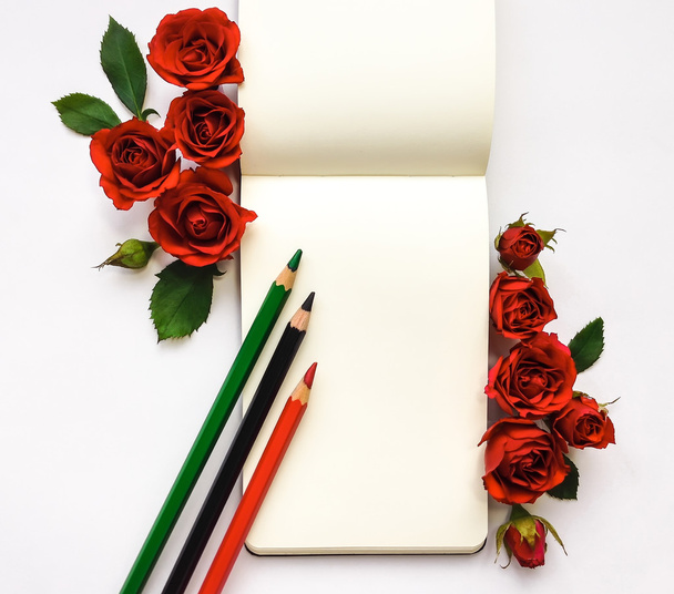 Colorful composition with sketchbook, roses and pencils. Flat lay on white table, top view - Zdjęcie, obraz