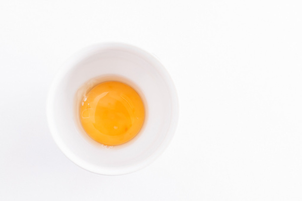 nyers tojás sárgáját egy tálba, egy fehér háttér - Fotó, kép