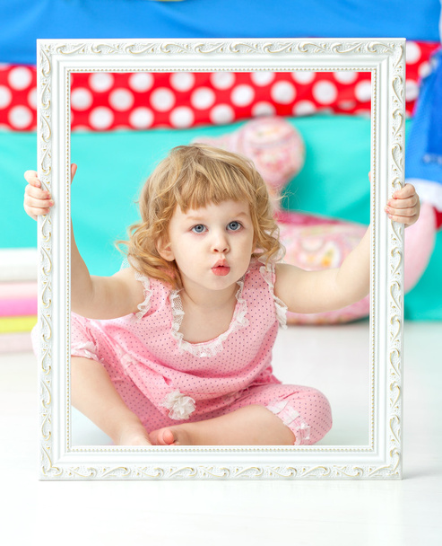 Little cute girl in a pink suit sitting on the floor and smiling over wooden white frame. - Fotó, kép