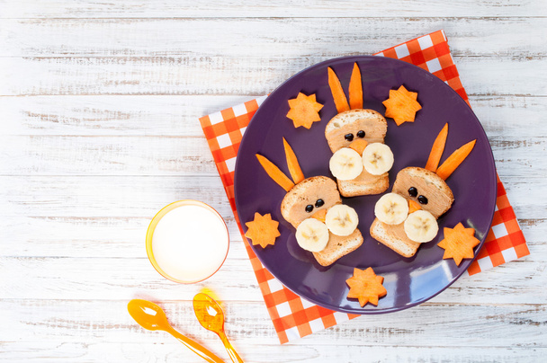 Дитячий сніданок з бутербродами та молоком. Смішний кролик для обличчя бутерброди з арахісовим маслом, бананом і морквою
 - Фото, зображення