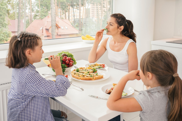 Madre e figlie che mangiano cibo sano in cucina
 - Foto, immagini