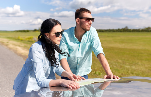 happy man and woman with road map on car hood - Photo, Image