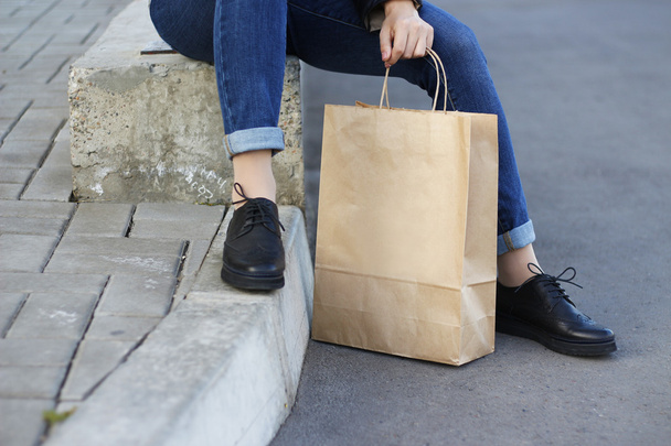 Девушка в красивых туфлях сидит рядом с бумажным пакетом
. - Фото, изображение