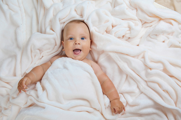 Caucasian baby boy covered with  towel joyfully smiles at camera - Foto, Imagen