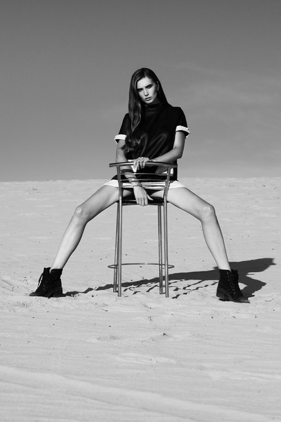 Creatieve schot in de woestijn. Een mooie sexy meisje in een zwarte jurk. T - Foto, afbeelding