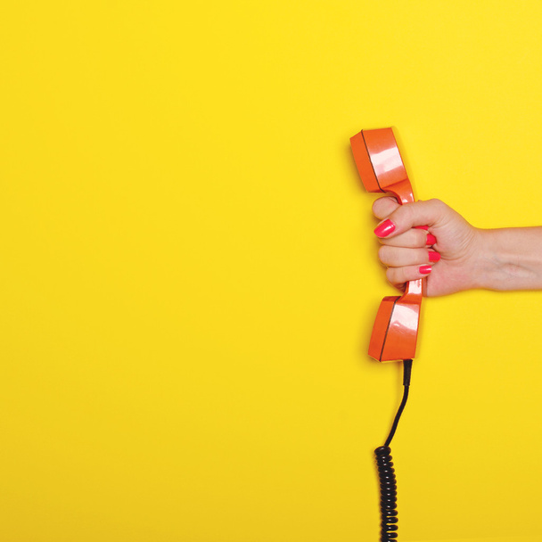 Woman hand holding retro orange phone tube against yellow backgr - Foto, imagen