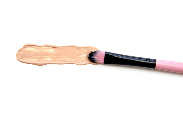 Close-up van make-up borstel met vlekkerig vloeibare foundation op witte achtergrond. Bovenaanzicht - Foto, afbeelding