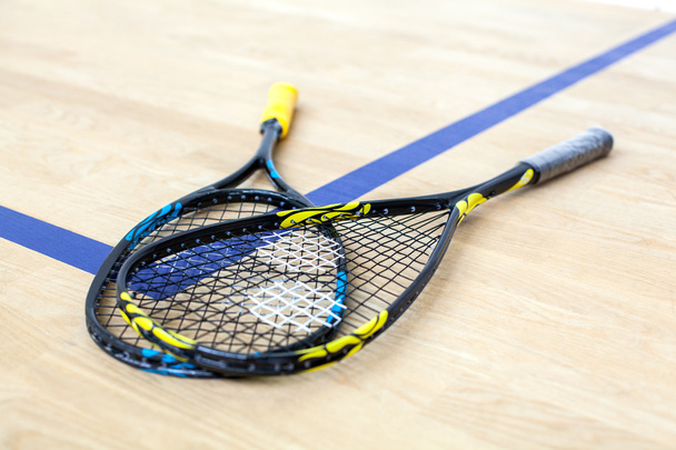 Желтые и синие теннисные ракетки лежат на деревянном корте
 - Фото, изображение