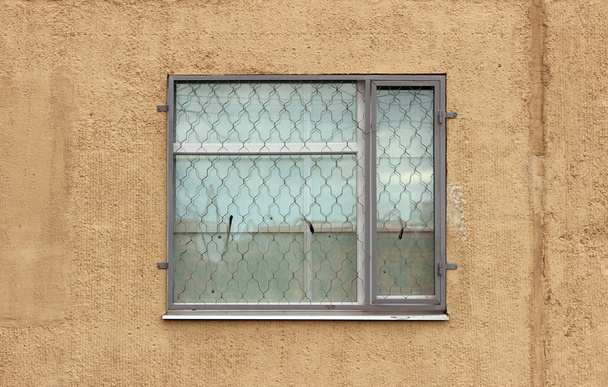 jedno szare okno z osłoną zabezpieczającą na pierwszym piętrze nowoczesnego budynku na beżowym tle. - Zdjęcie, obraz