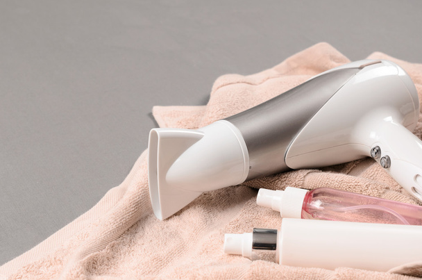 Beyaz saç kurutma makinesi ve bej havlu üzerinde iki saç spreyi - Fotoğraf, Görsel