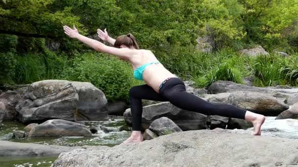 Νέοι και σπορ κορίτσι τεντώνει το πόδι πάνω σε ένα βράχο στη μέση ενός ποταμού στο βουνό. - Πλάνα, βίντεο
