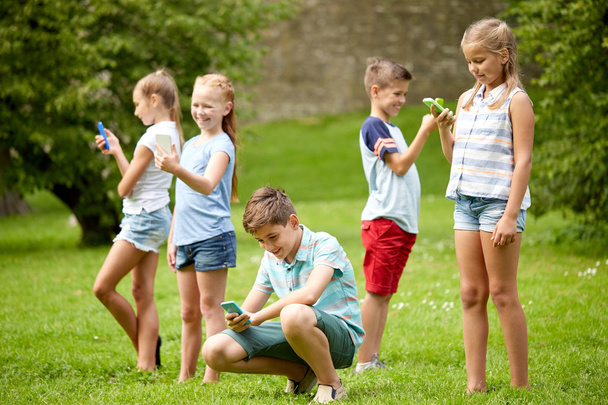 niños con smartphones jugando en el parque de verano
 - Foto, imagen