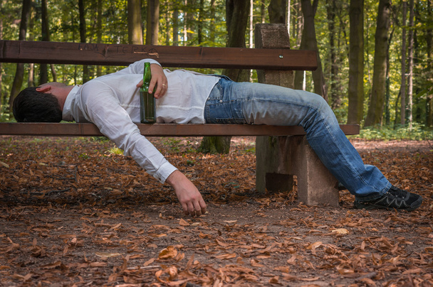Hombre borracho dormido en un banco del parque con botellas de cerveza
 - Foto, Imagen