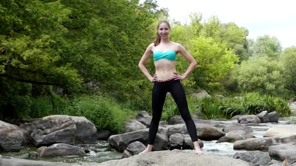 Jeune fille sportive s'étire la jambe sur un rocher au milieu d'une rivière de montagne
. - Séquence, vidéo
