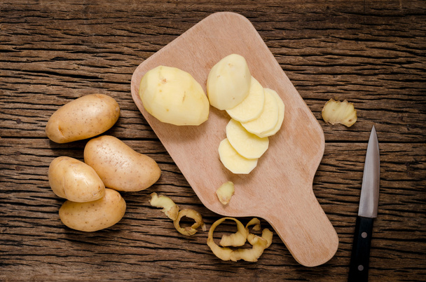 Pelez et épluchez les pommes de terre fraîches sur une planche à découper en bois
. - Photo, image
