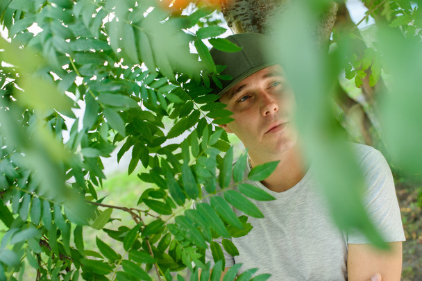 jovem cara físico padrão posando na rua em um fundo de arbustos verdes
 - Foto, Imagem