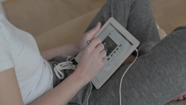 Beautiful girl in a white T-shirt with a tablet computer on a light sofa. - Video, Çekim