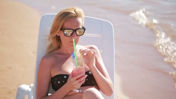 woman drinking a cocktail on the beach. woman sunbathing by the sea - Кадри, відео