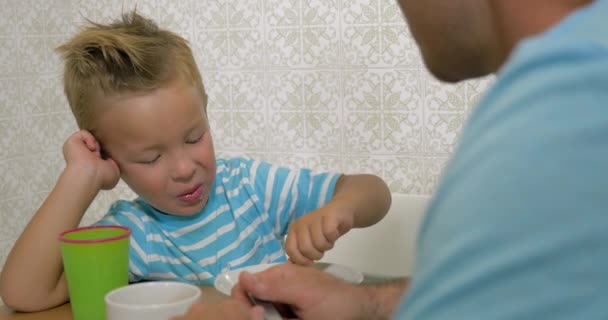 Son speaking with father and eat using a spoon and smiling - Filmati, video
