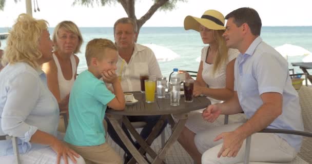Duża rodzina siedzi przy stole na wybrzeżu morza w mieście Perea, Grecja - Materiał filmowy, wideo