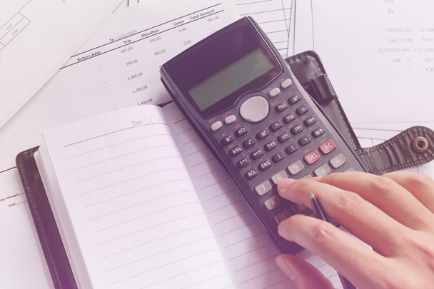 savings, finances, economy and office concept. Business people counting on calculator, notebook, holding pen in hand, sitting at the table. Close up of hands and stationery, soft focus - Photo, Image