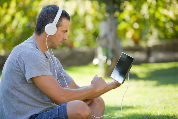 молодой человек отдыхает с планшетным компьютером, слушая музыку в наушниках
 - Фото, изображение
