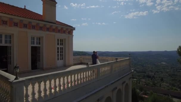 Man and woman stand embracing on balcony view from above flyover. Couple in love have romantic date at ancient house terrace with mountains view at background Europe France. Wedding day destination - Πλάνα, βίντεο