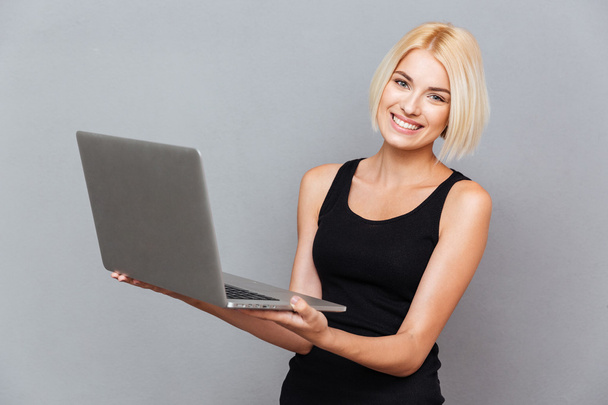 Portrait of cheerful charming young woman standing and using laptop - Foto, Imagem