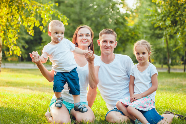 Young happy family of four sitting in the park on the grass - Fotografie, Obrázek