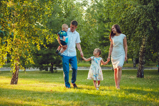 Feliz familia joven de cuatro personas caminando y divirtiéndose en el parque
 - Foto, Imagen